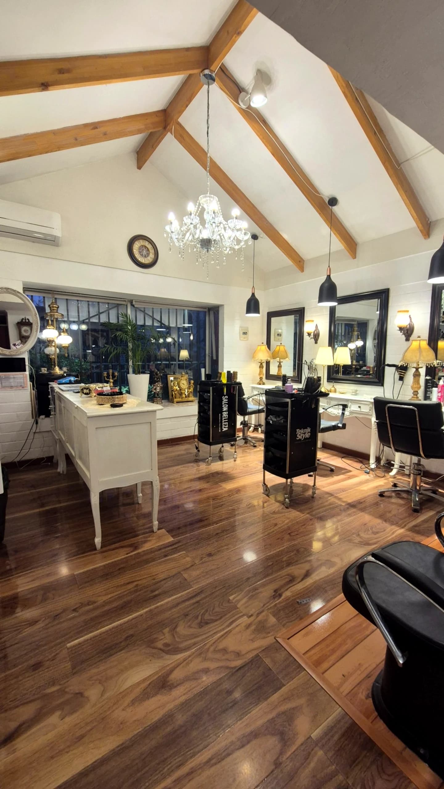 Sala principal de Peluquería Gianinna Canessa: techo a dos aguas con vigas de madera, araña de cristal, tocadores con espejos y piso de nogal